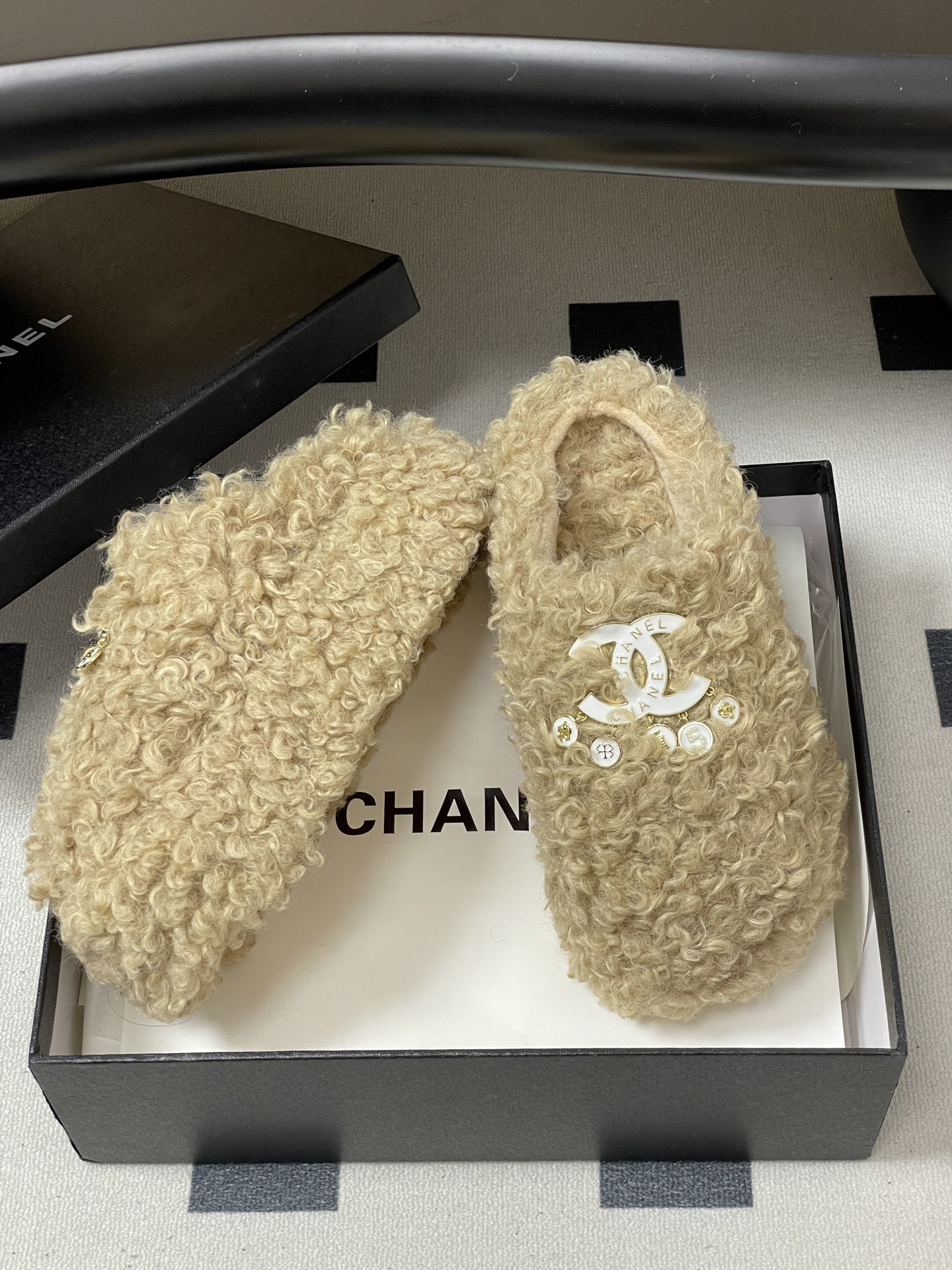 Pair of beige curly faux fur platform slippers featuring a white designer logo with hanging pearl charms on a black surface. - Hình 6