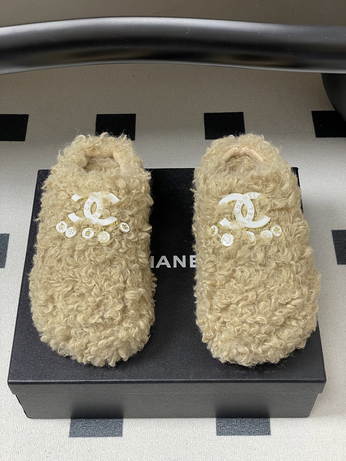Pair of beige curly faux fur platform slippers featuring a white designer logo with hanging pearl charms on a black surface. - Hình 5