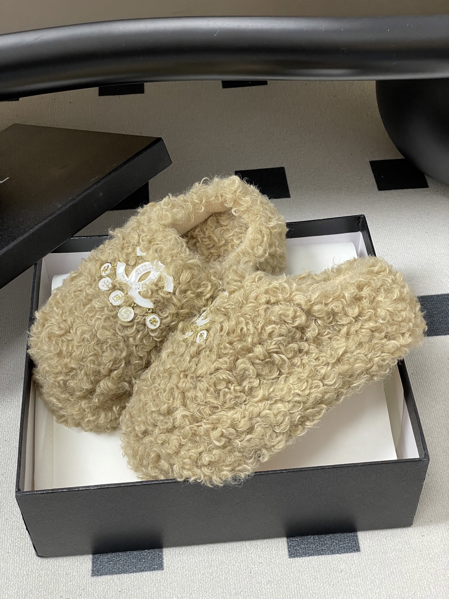 Pair of beige curly faux fur platform slippers featuring a white designer logo with hanging pearl charms on a black surface. - Hình 4