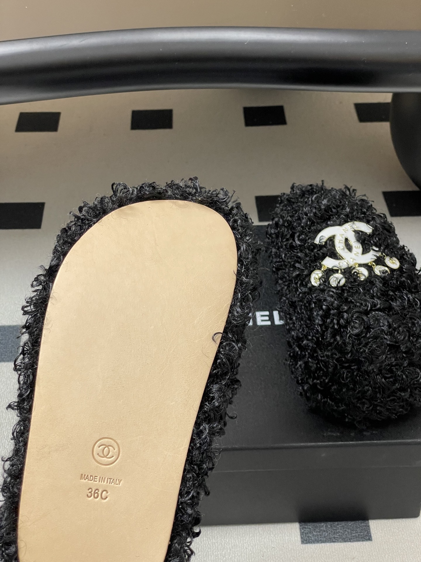 Pair of black curly faux fur loafers with white interlocking logo and dangling charms on a black surface. - Hình 8