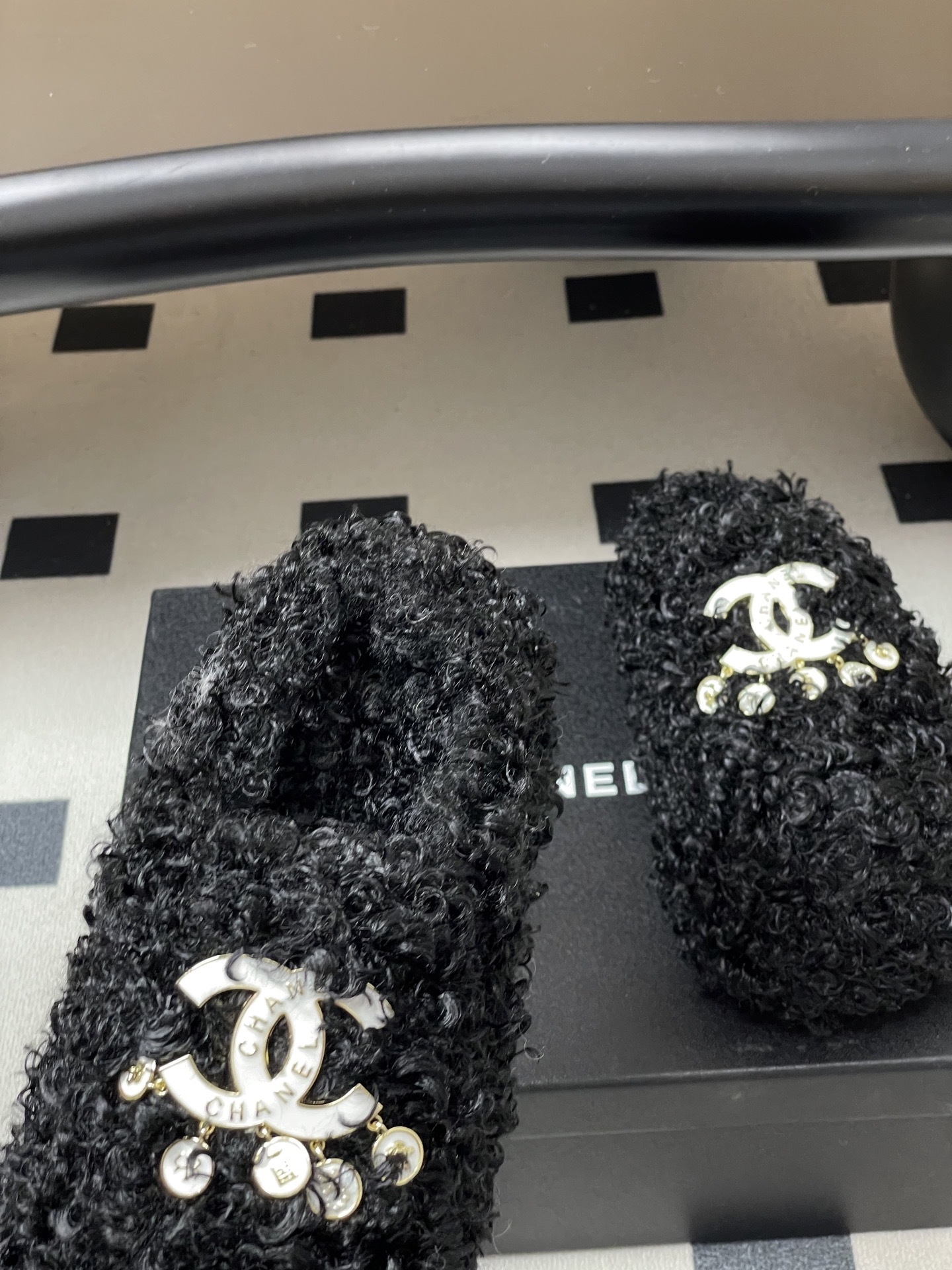 Pair of black curly faux fur loafers with white interlocking logo and dangling charms on a black surface. - Hình 7