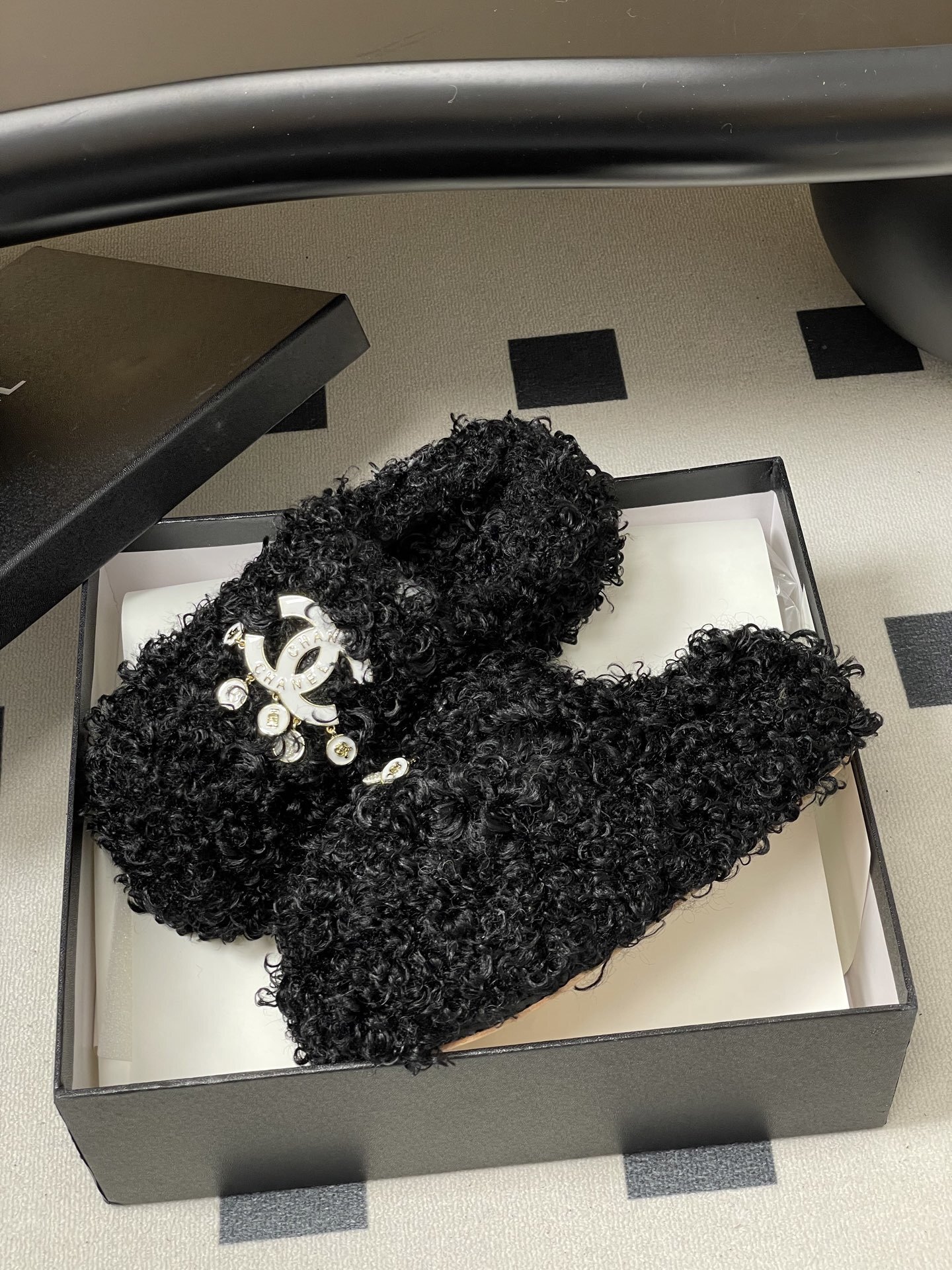 Pair of black curly faux fur loafers with white interlocking logo and dangling charms on a black surface. - Hình 4