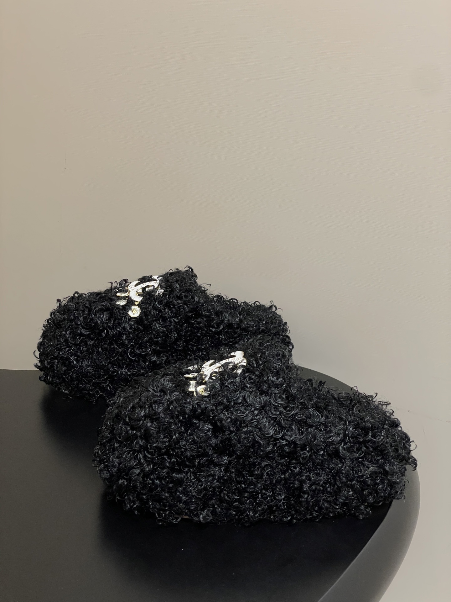 Pair of black curly faux fur loafers with white interlocking logo and dangling charms on a black surface. - Hình 3