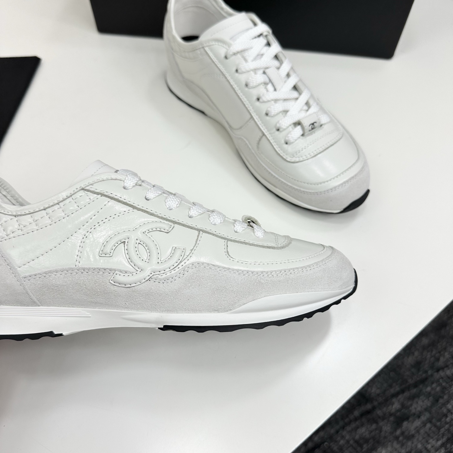 Side view of white Chanel low-top sneakers featuring leather and suede panels with the iconic CC logo on a black box. - Hình 9