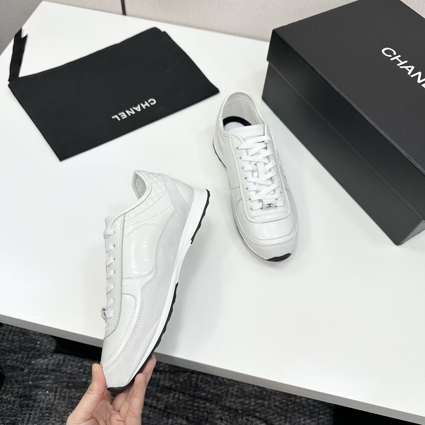 Side view of white Chanel low-top sneakers featuring leather and suede panels with the iconic CC logo on a black box. - Hình 8