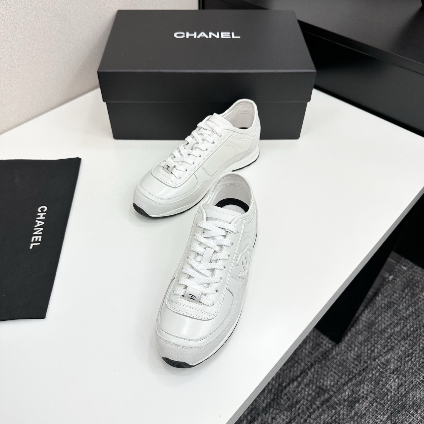 Side view of white Chanel low-top sneakers featuring leather and suede panels with the iconic CC logo on a black box. - Hình 5