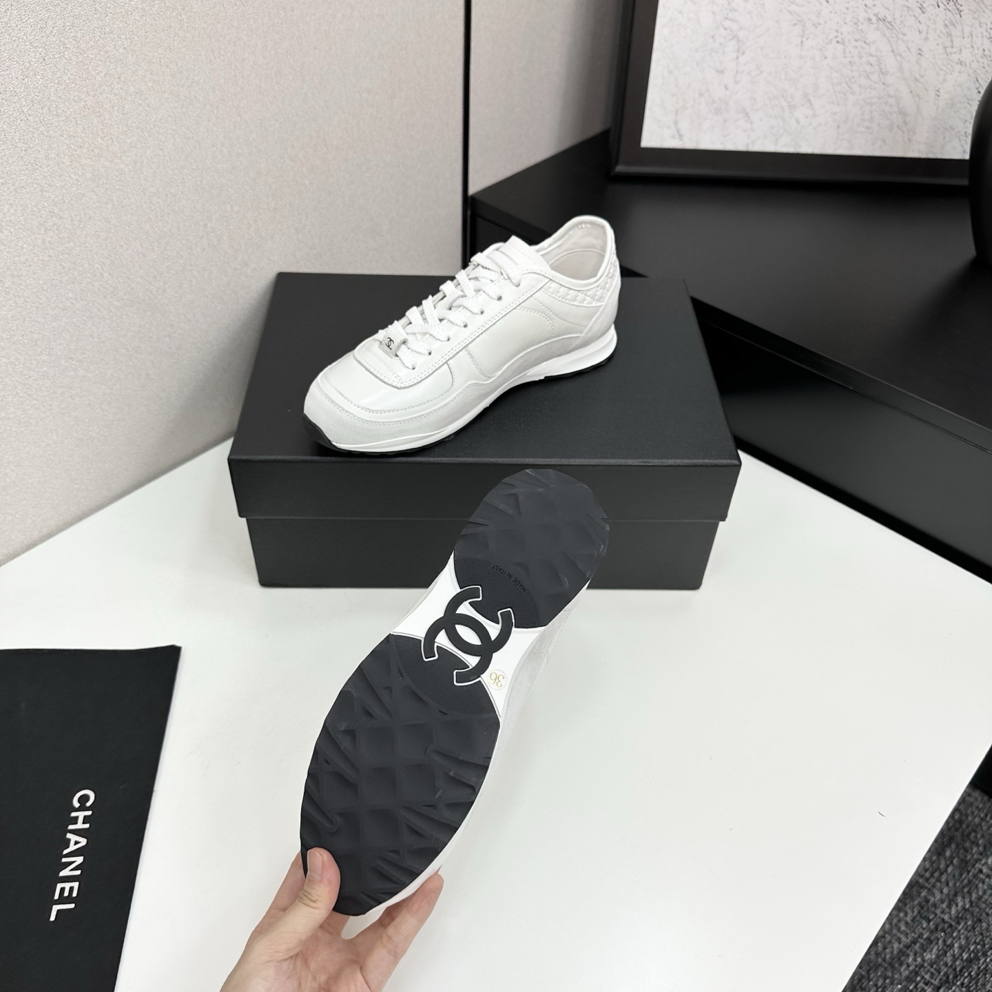Side view of white Chanel low-top sneakers featuring leather and suede panels with the iconic CC logo on a black box. - Hình 4