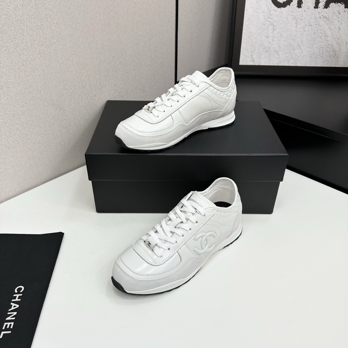 Side view of white Chanel low-top sneakers featuring leather and suede panels with the iconic CC logo on a black box. - Hình 2