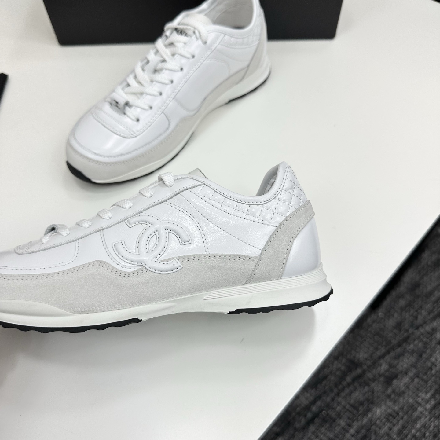 Side view of luxury white Chanel sneakers with quilted leather and interlocking CC logo on a black box. - Hình 9