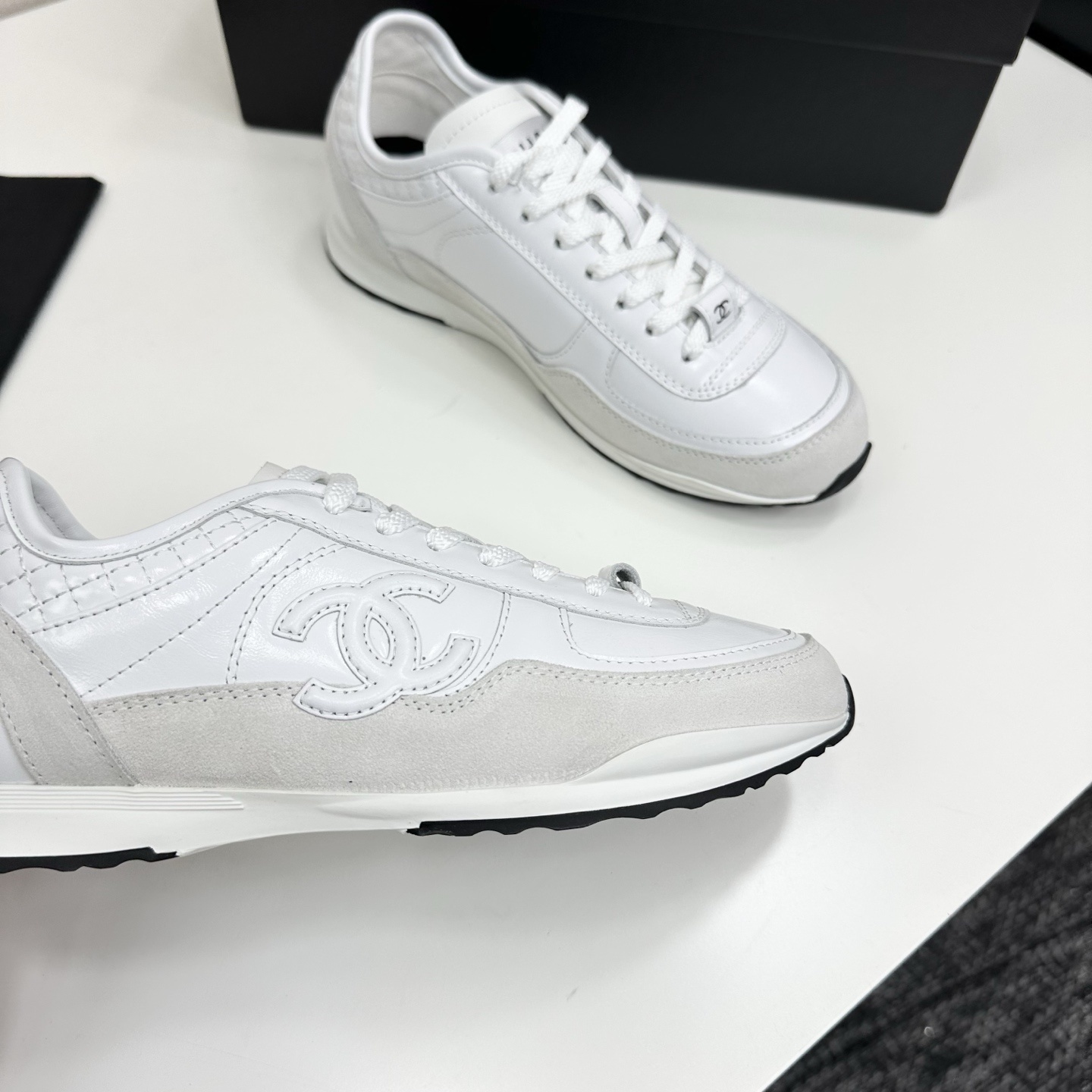 Side view of luxury white Chanel sneakers with quilted leather and interlocking CC logo on a black box. - Hình 8