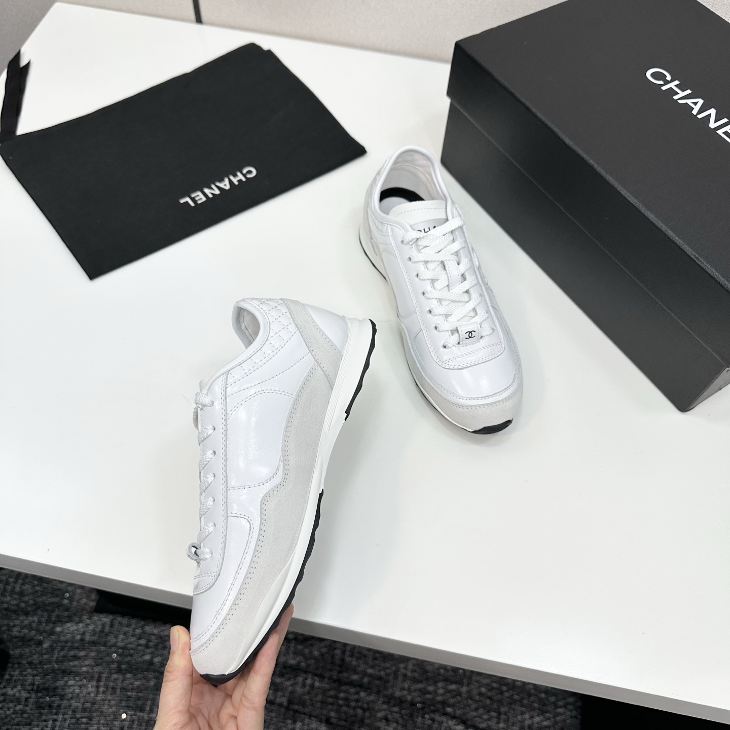 Side view of luxury white Chanel sneakers with quilted leather and interlocking CC logo on a black box. - Hình 7