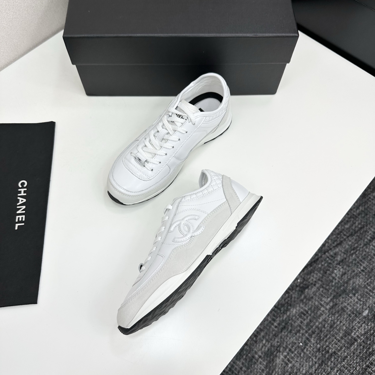 Side view of luxury white Chanel sneakers with quilted leather and interlocking CC logo on a black box. - Hình 5