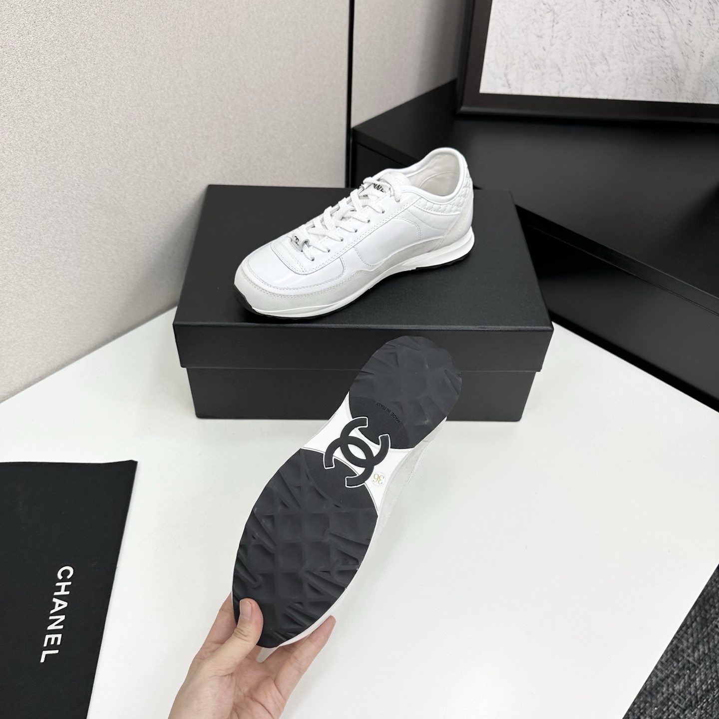 Side view of luxury white Chanel sneakers with quilted leather and interlocking CC logo on a black box. - Hình 4