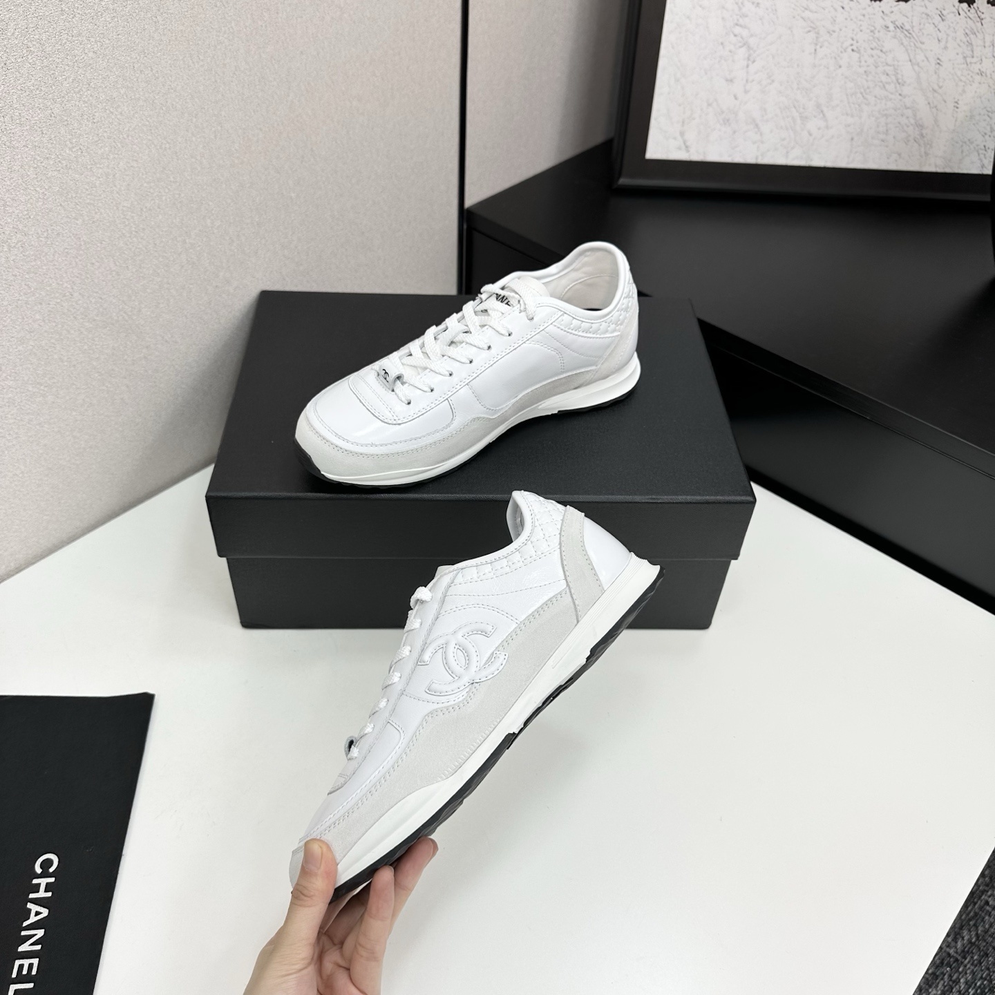 Side view of luxury white Chanel sneakers with quilted leather and interlocking CC logo on a black box. - Hình 3