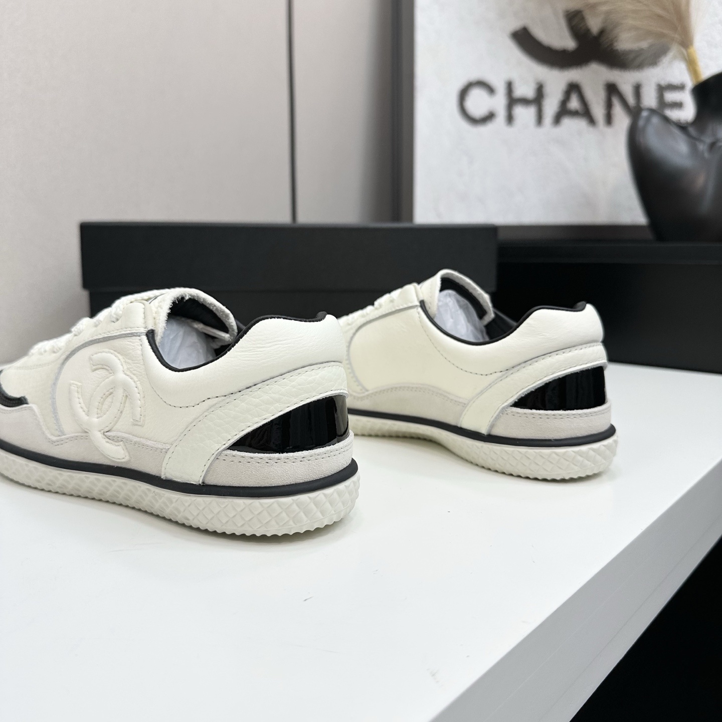 Pair of Chanel white leather sneakers with black patent toe caps and interlocking CC logo on a black display box - Hình 8