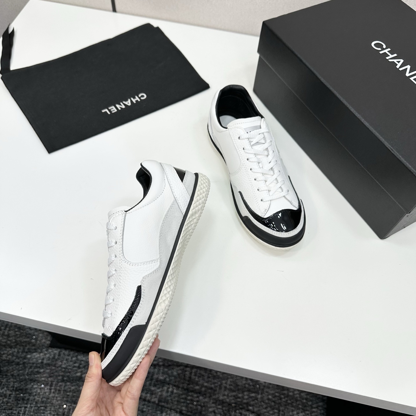 Side view of white Chanel calfskin sneakers with black patent leather details and white interlocking CC logo on a black box. - Hình 8