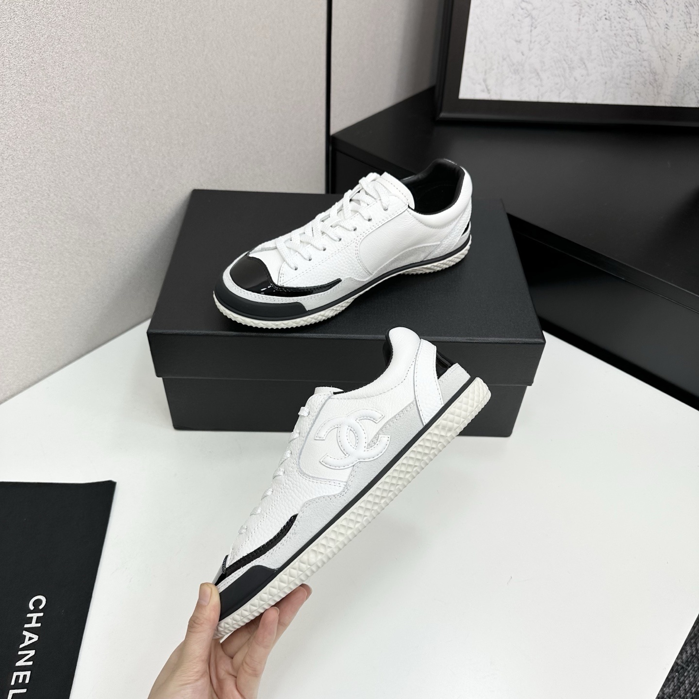 Side view of white Chanel calfskin sneakers with black patent leather details and white interlocking CC logo on a black box. - Hình 3