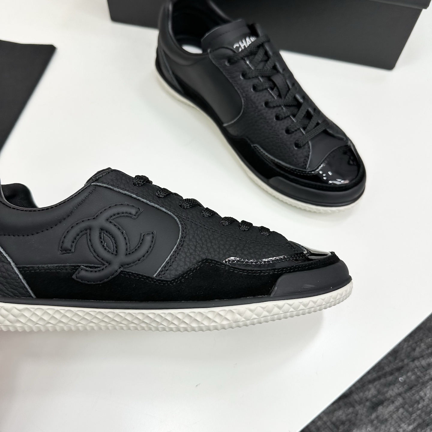 A pair of premium black Chanel leather sneakers with a white textured sole and embossed CC logo displayed on a luxury black box. - Hình 9