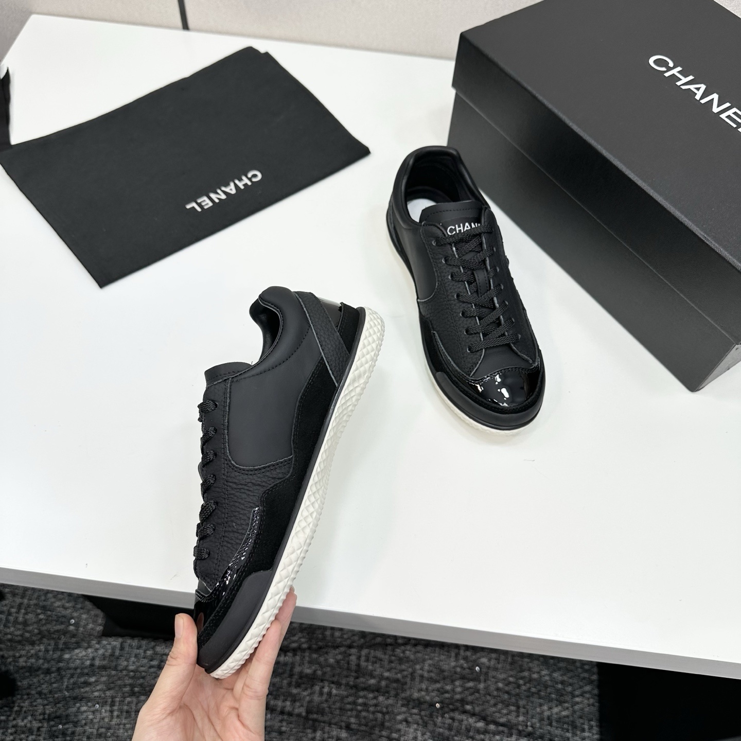 A pair of premium black Chanel leather sneakers with a white textured sole and embossed CC logo displayed on a luxury black box. - Hình 8