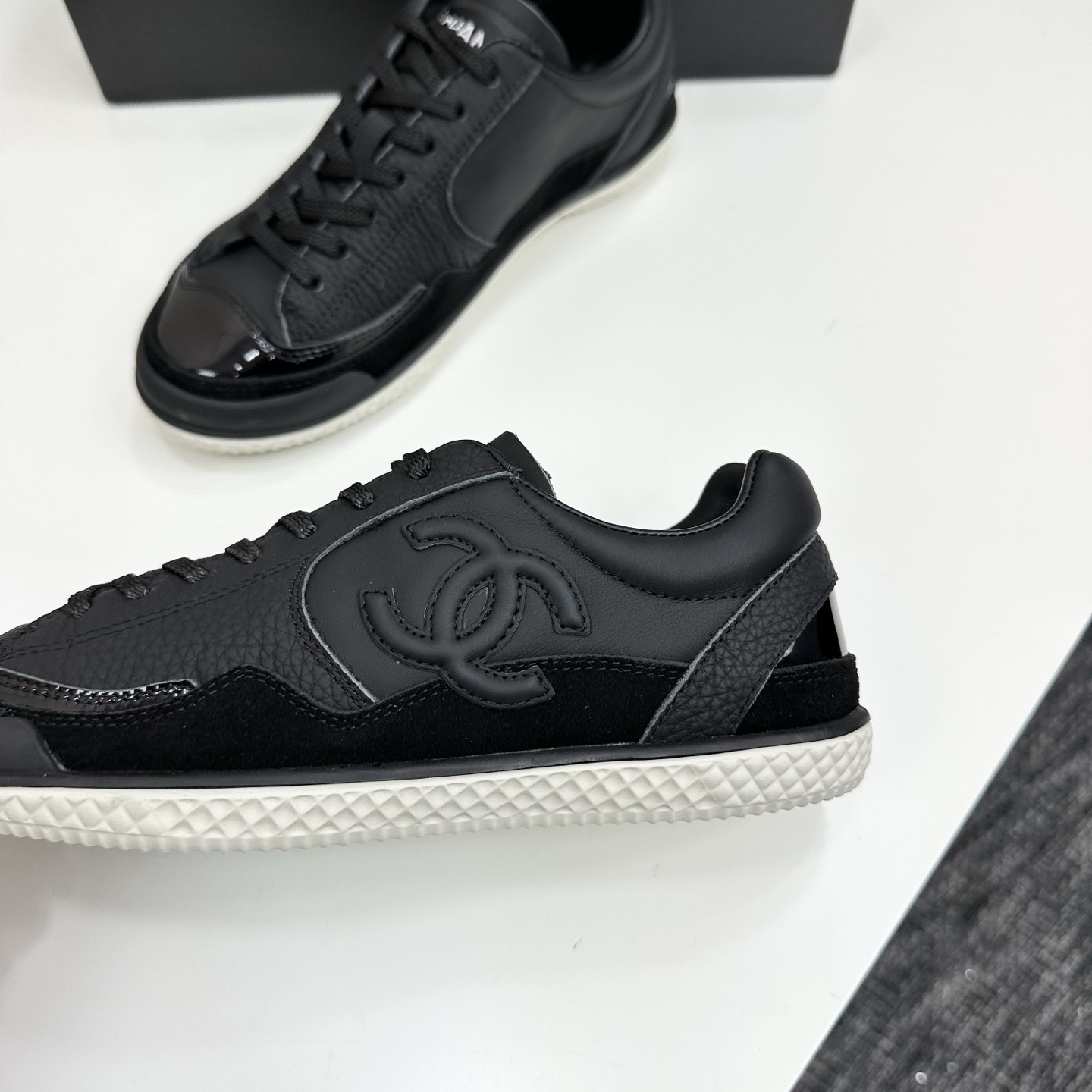 A pair of premium black Chanel leather sneakers with a white textured sole and embossed CC logo displayed on a luxury black box. - Hình 7