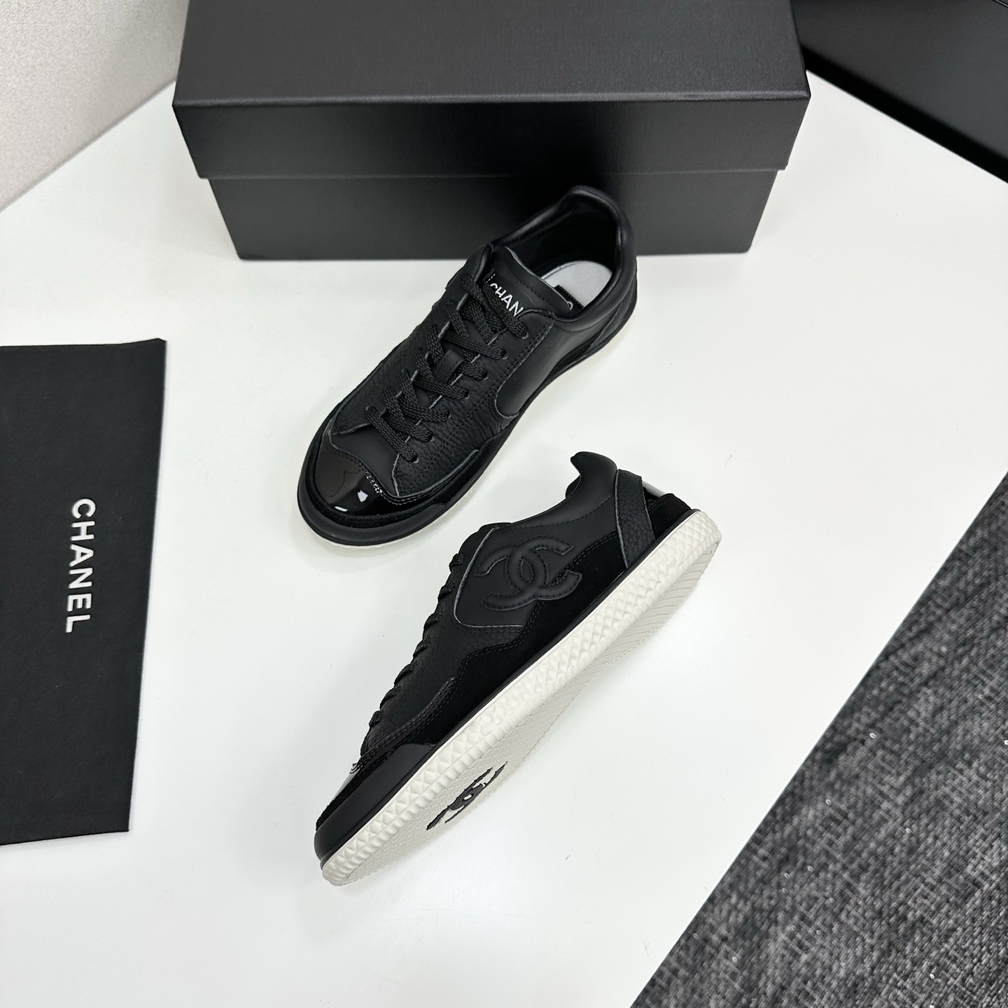 A pair of premium black Chanel leather sneakers with a white textured sole and embossed CC logo displayed on a luxury black box. - Hình 6