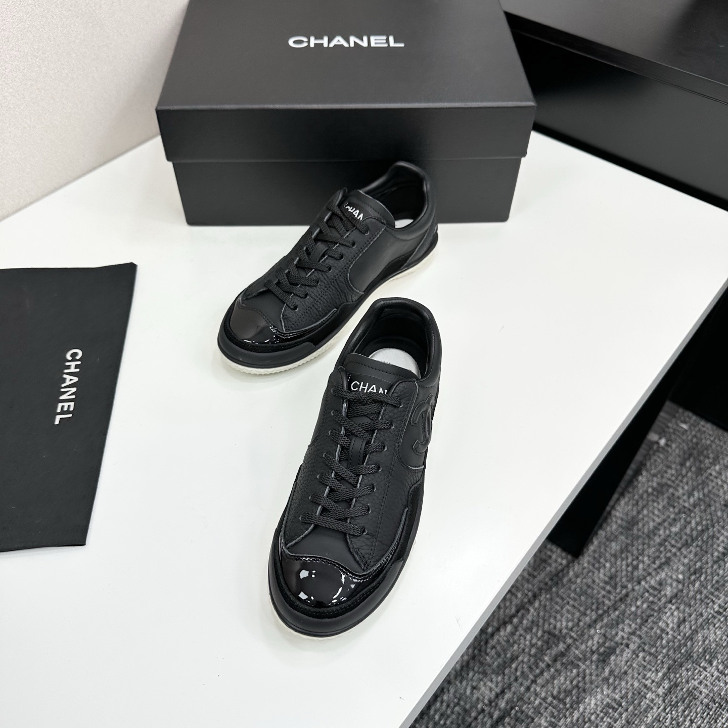 A pair of premium black Chanel leather sneakers with a white textured sole and embossed CC logo displayed on a luxury black box. - Hình 5