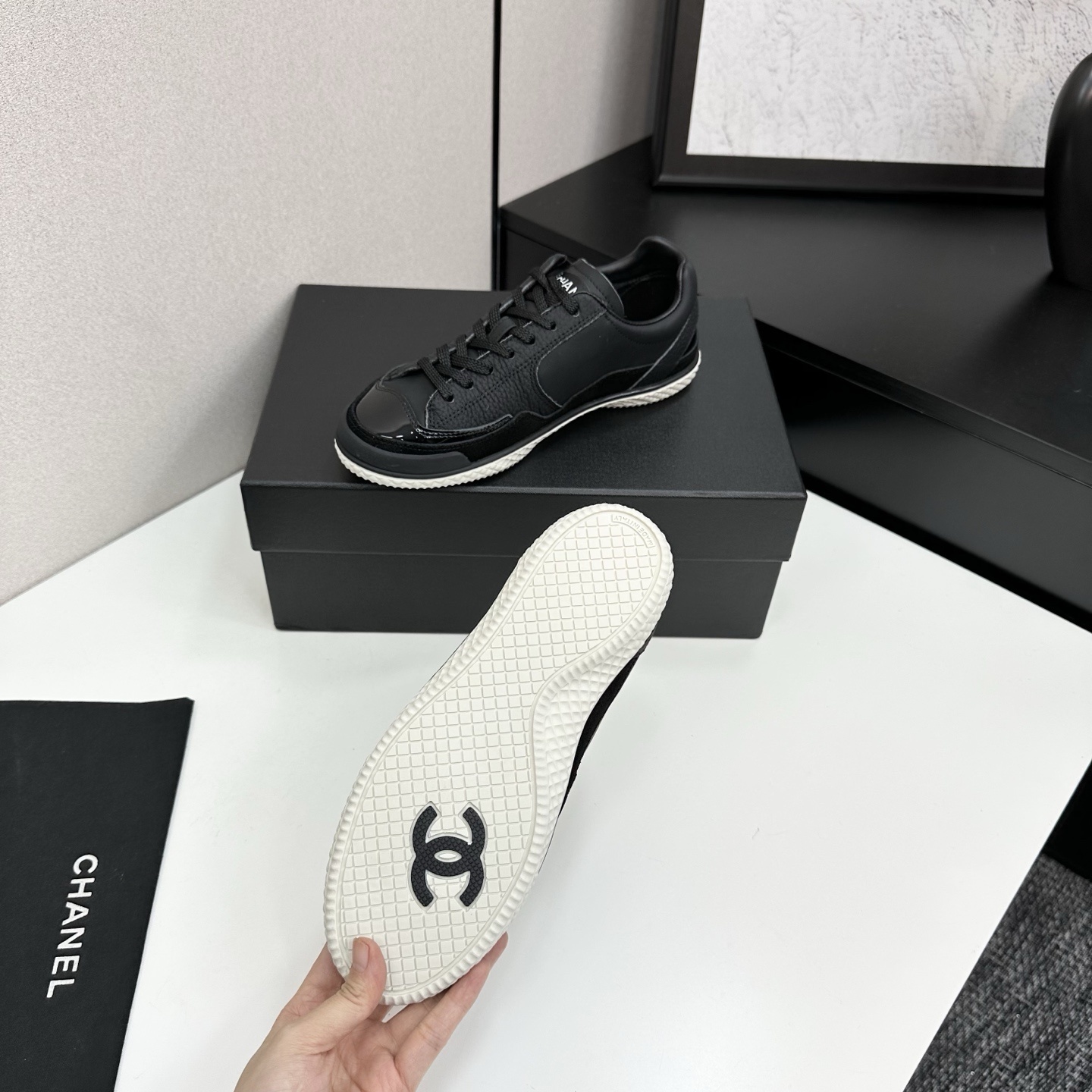A pair of premium black Chanel leather sneakers with a white textured sole and embossed CC logo displayed on a luxury black box. - Hình 4