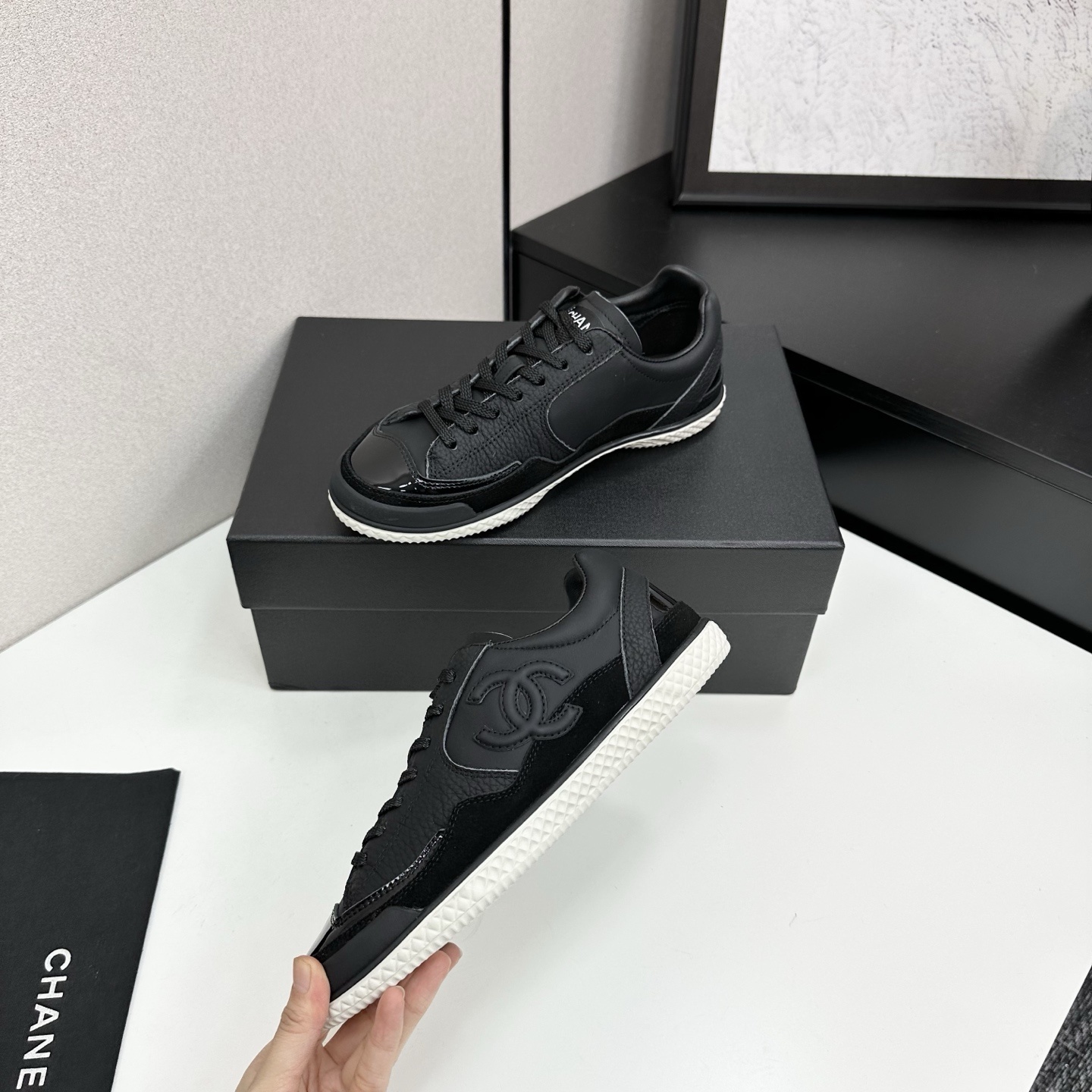 A pair of premium black Chanel leather sneakers with a white textured sole and embossed CC logo displayed on a luxury black box. - Hình 3