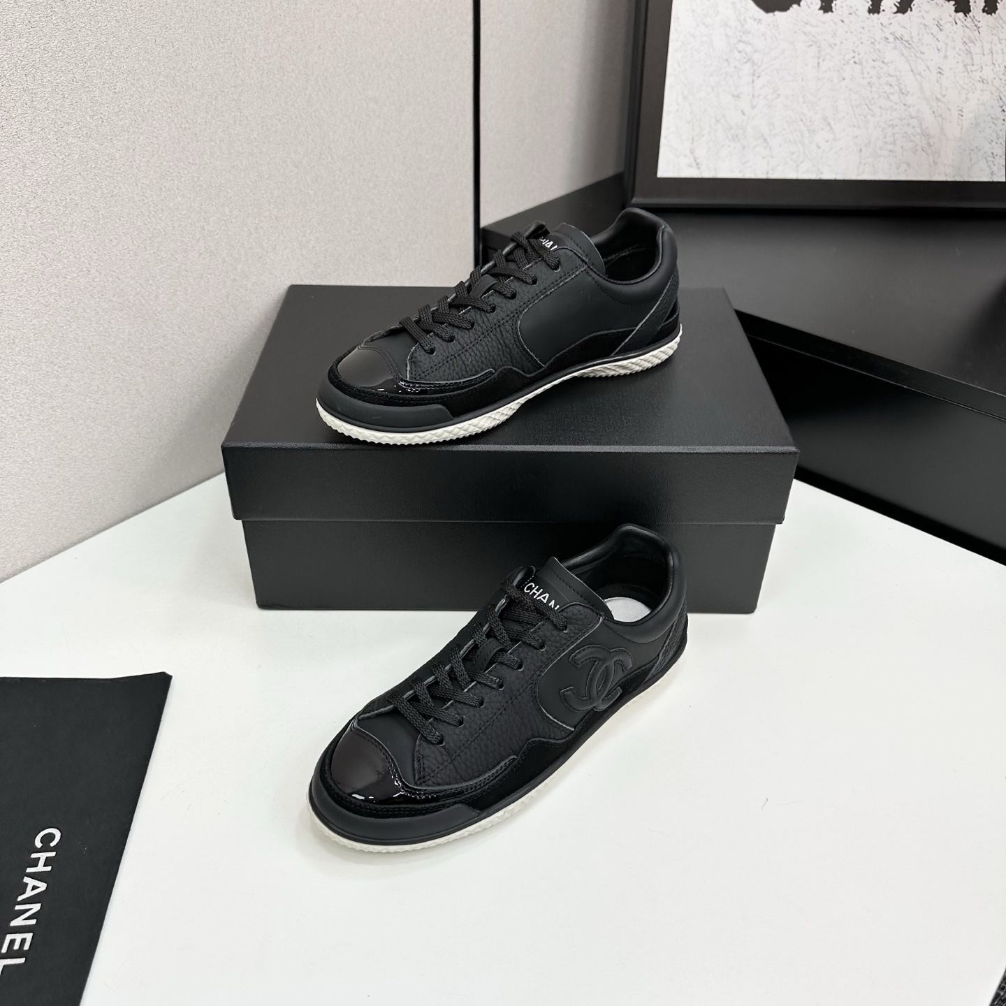 A pair of premium black Chanel leather sneakers with a white textured sole and embossed CC logo displayed on a luxury black box. - Hình 2