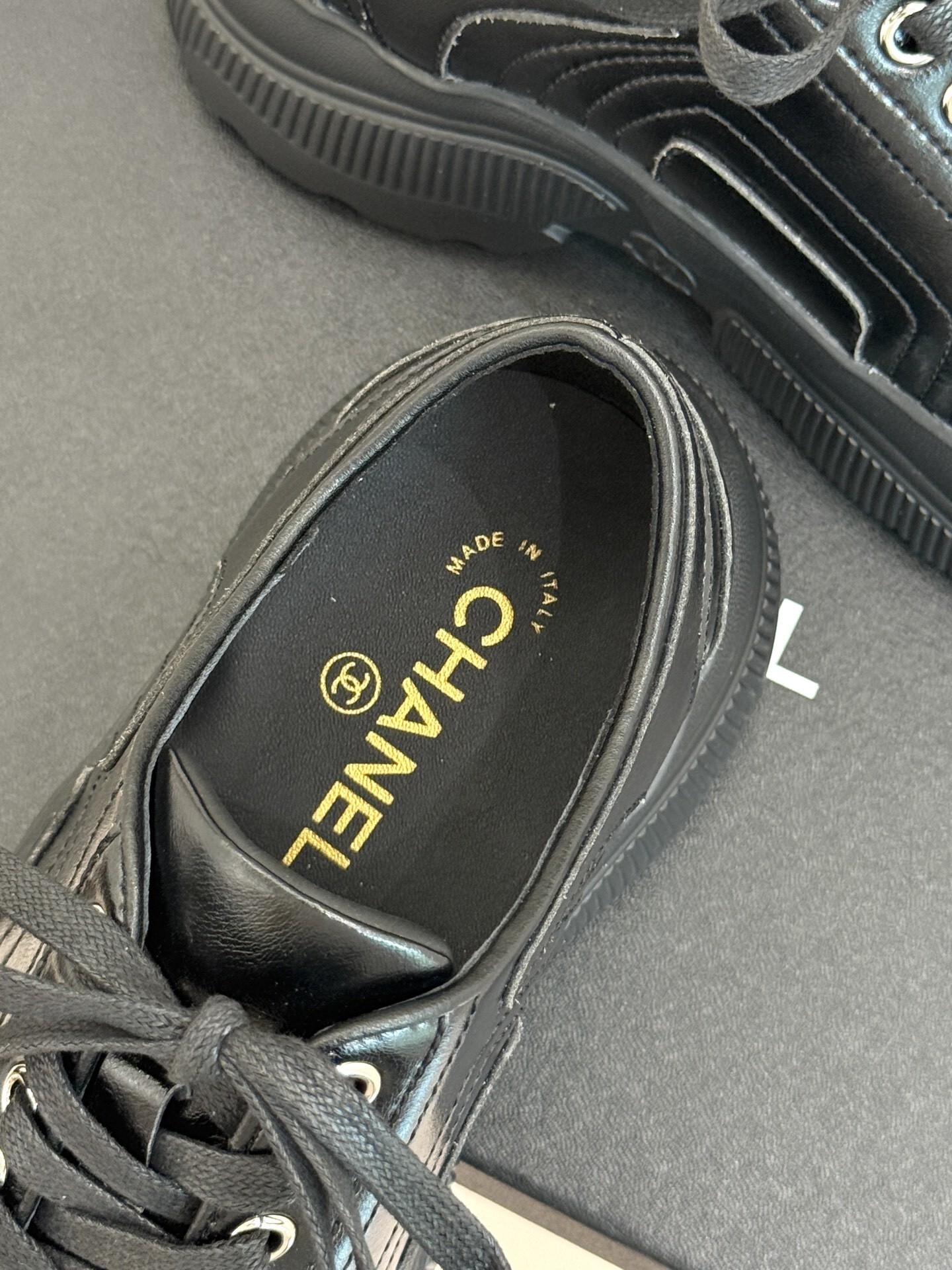 A pair of black Chanel leather platform sneakers with embossed CC logo on a black box, styled with a white tweed jacket and black quilted bag. - Hình 8