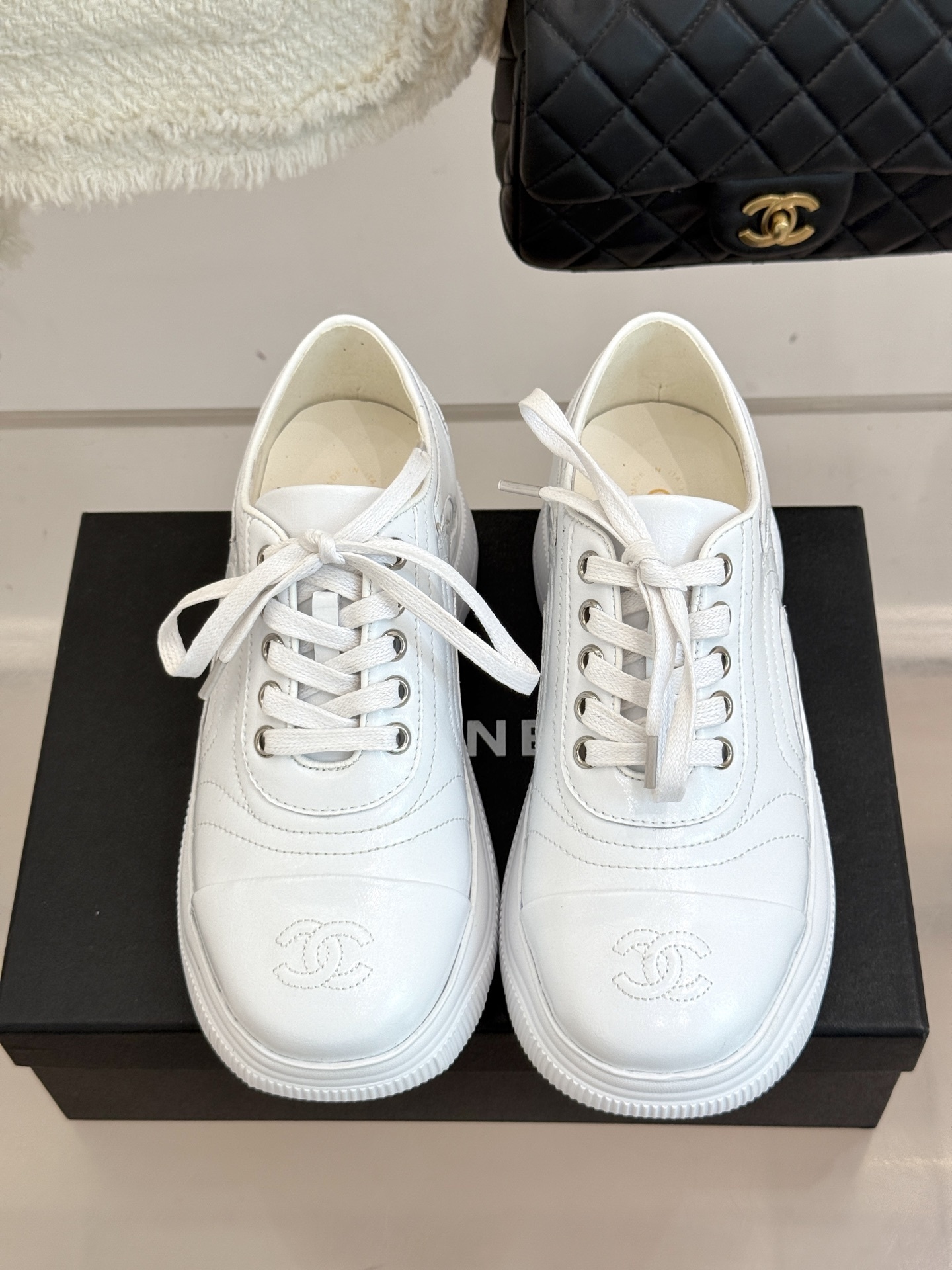 A pair of luxury white leather platform sneakers with embossed logo sitting on a black box. - Hình 4