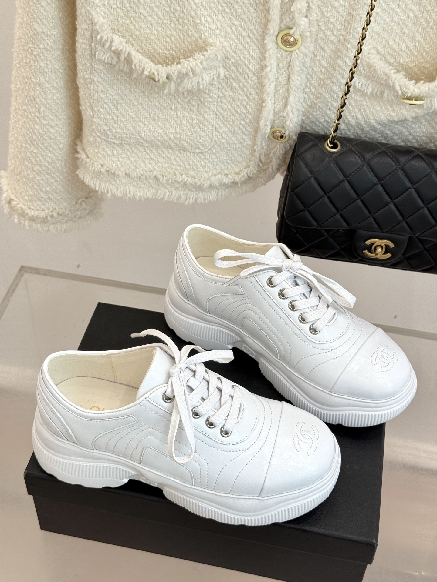 A pair of luxury white leather platform sneakers with embossed logo sitting on a black box. - Hình 3