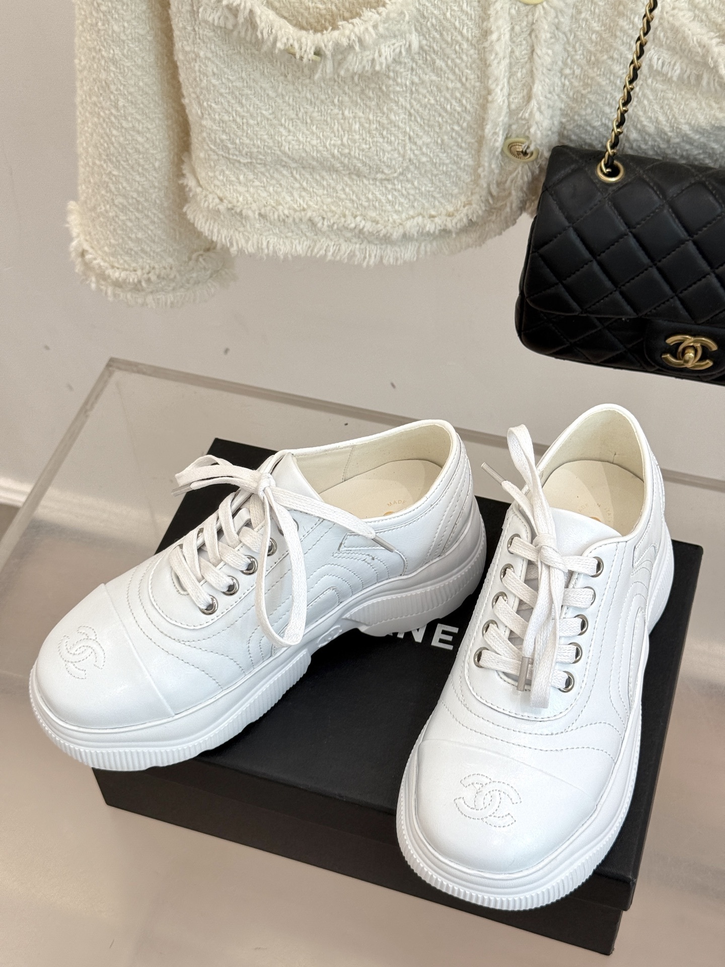 A pair of luxury white leather platform sneakers with embossed logo sitting on a black box. - Hình 2