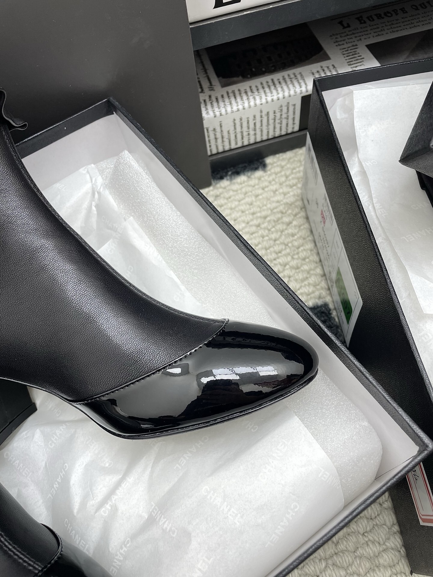 Pair of black Chanel leather ankle boots with ruffle trim and patent leather toe cap on a white surface. - Hình 10