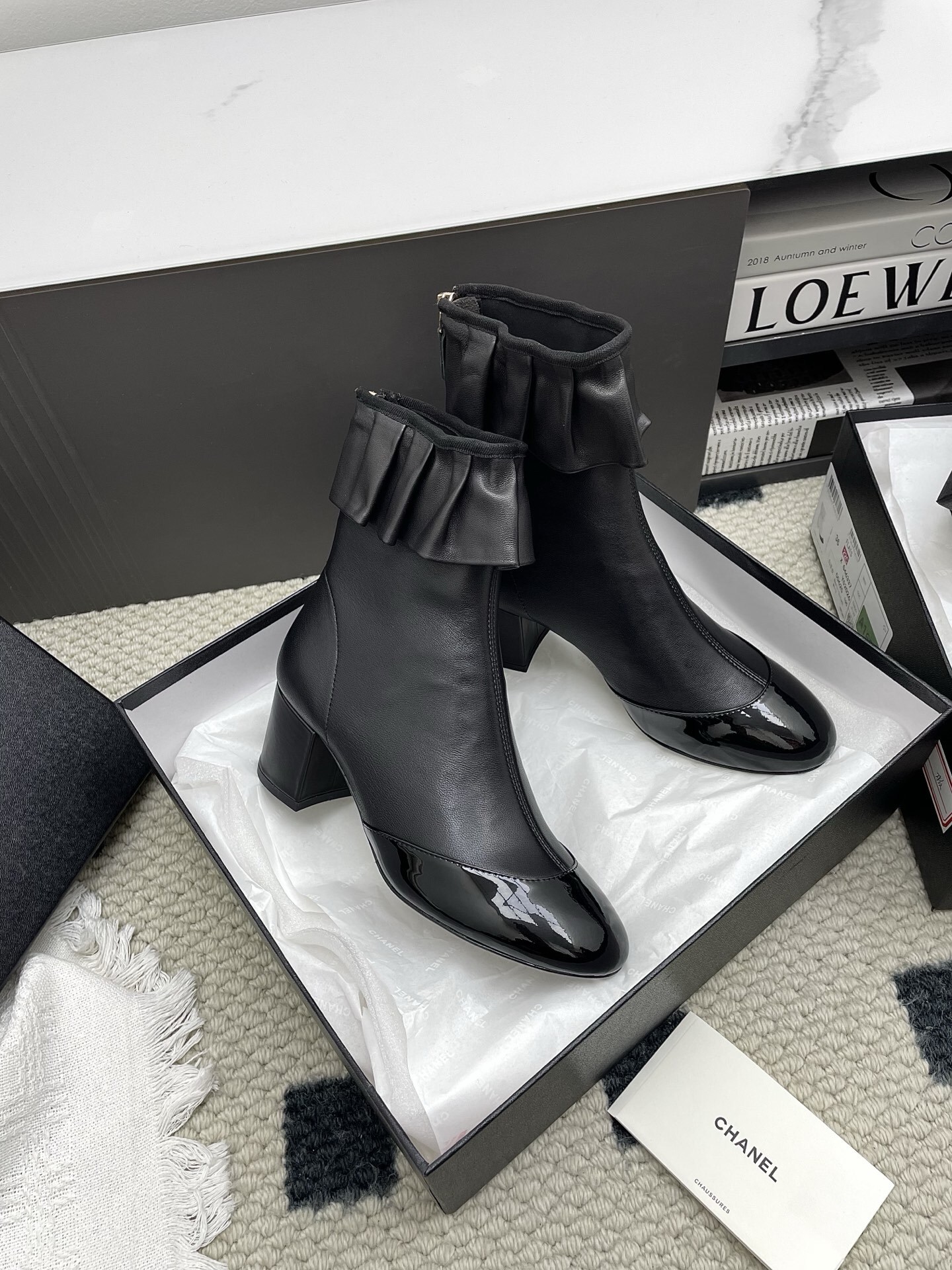 Pair of black Chanel leather ankle boots with ruffle trim and patent leather toe cap on a white surface. - Hình 8
