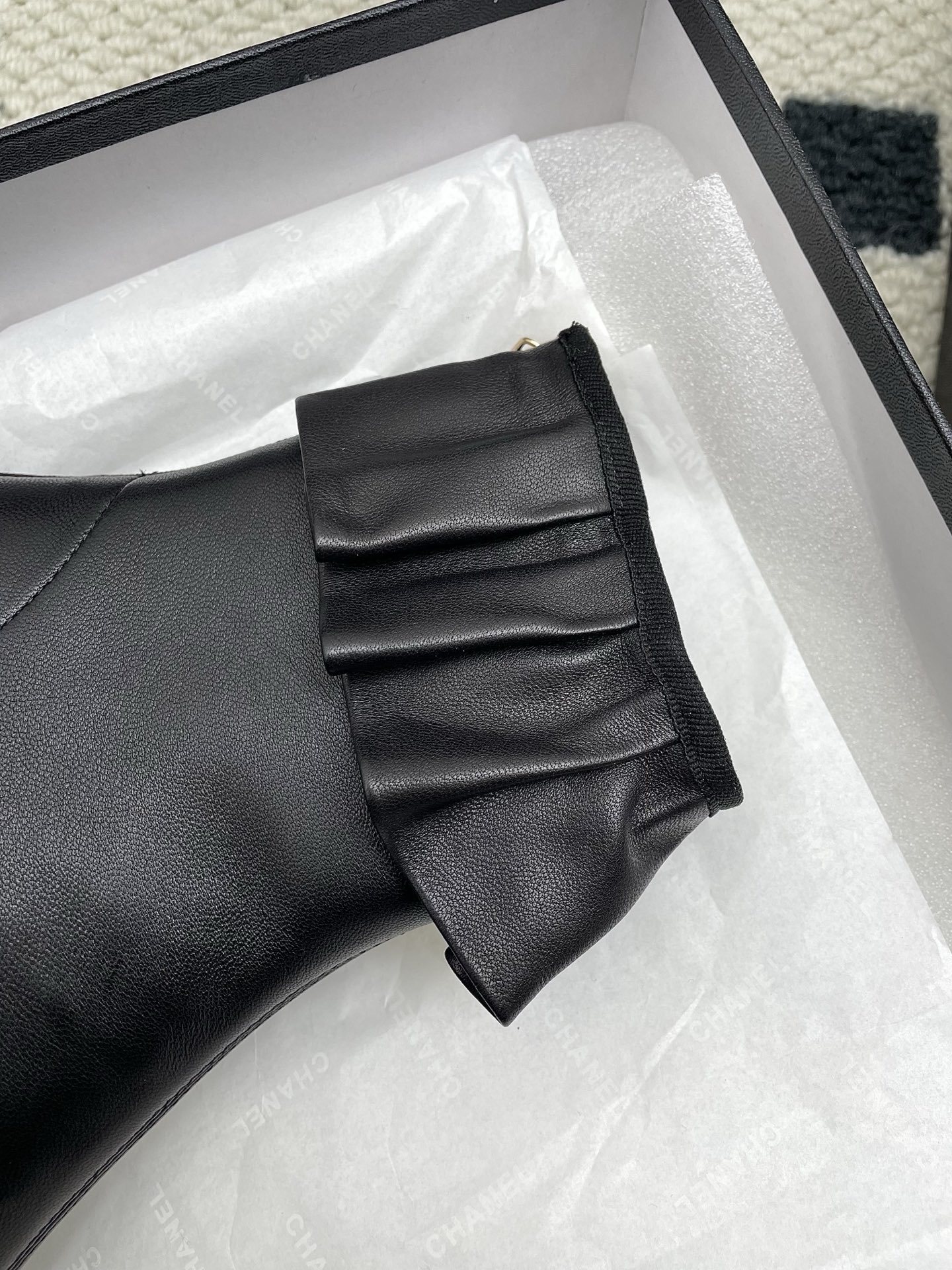 Pair of black Chanel leather ankle boots with ruffle trim and patent leather toe cap on a white surface. - Hình 7