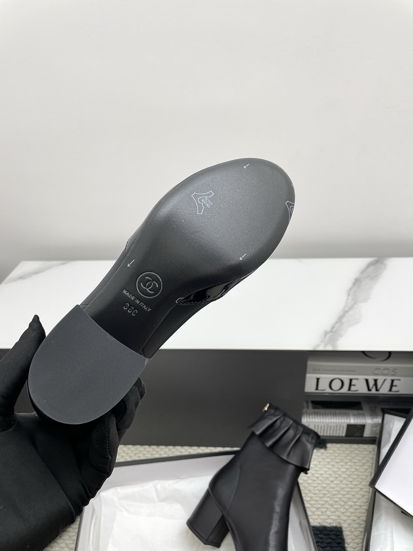 Pair of black Chanel leather ankle boots with ruffle trim and patent leather toe cap on a white surface. - Hình 3