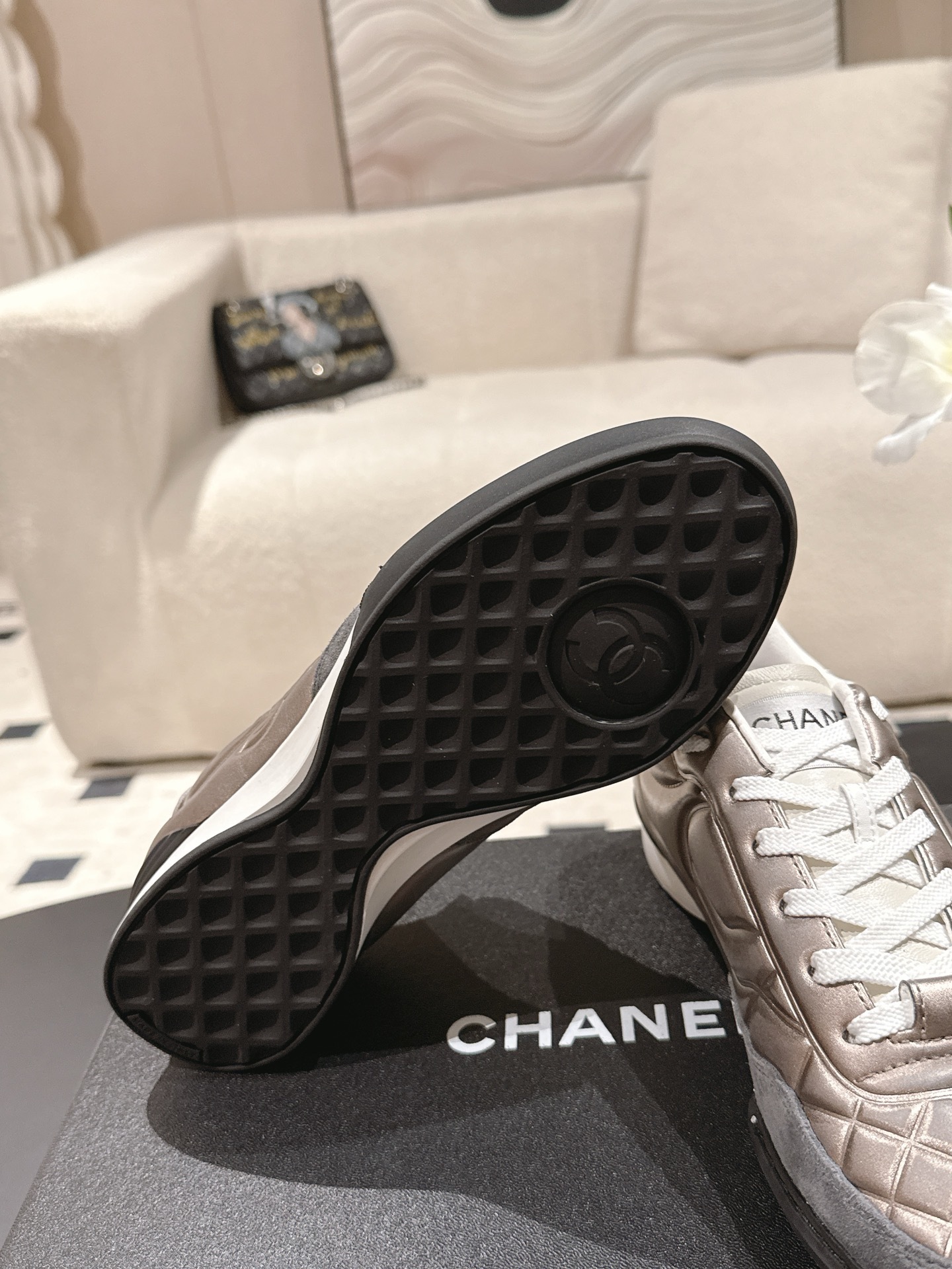 A pair of Chanel quilted metallic leather sneakers in champagne bronze resting on a black designer box - Hình 9