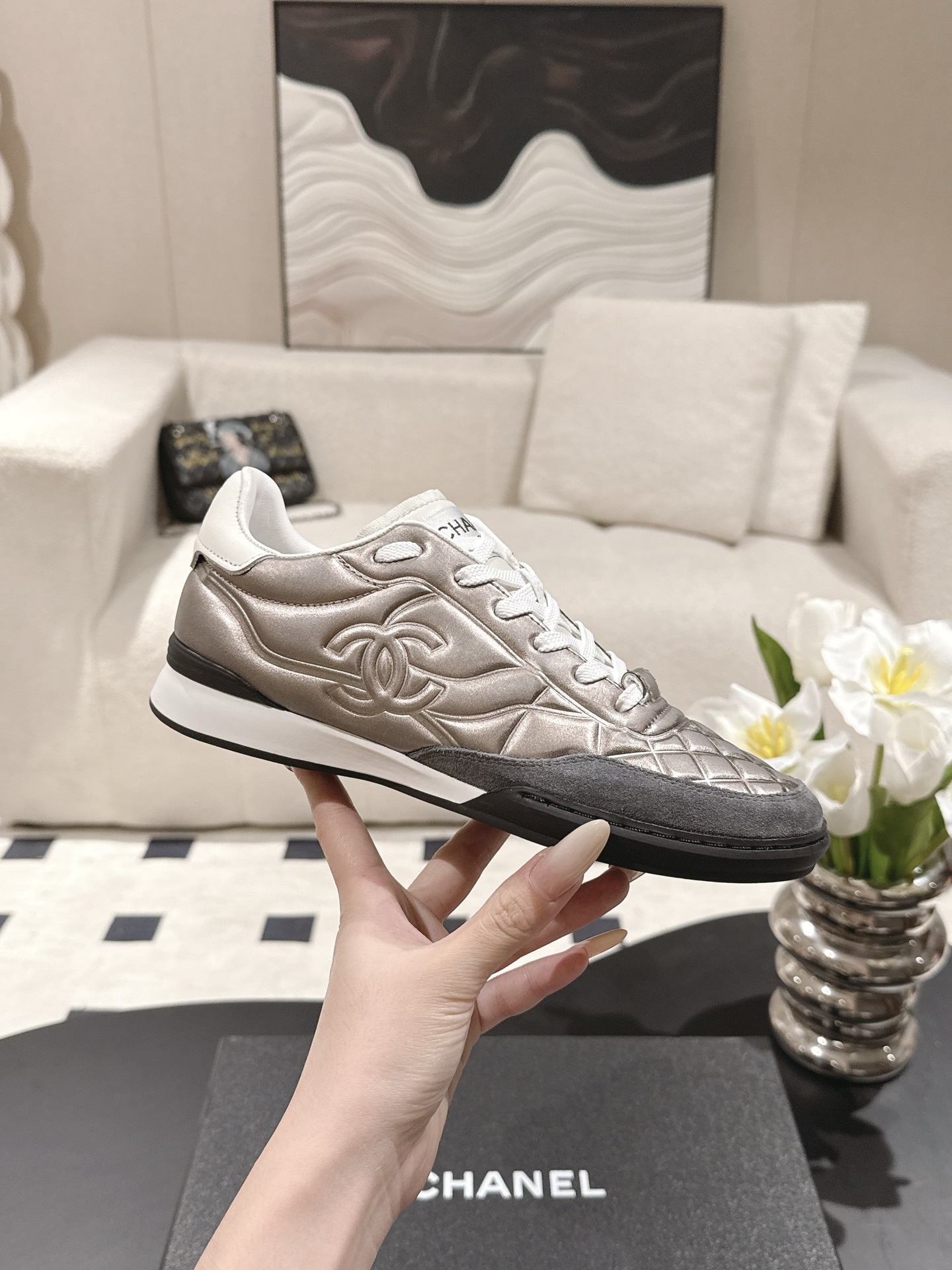 A pair of Chanel quilted metallic leather sneakers in champagne bronze resting on a black designer box - Hình 5