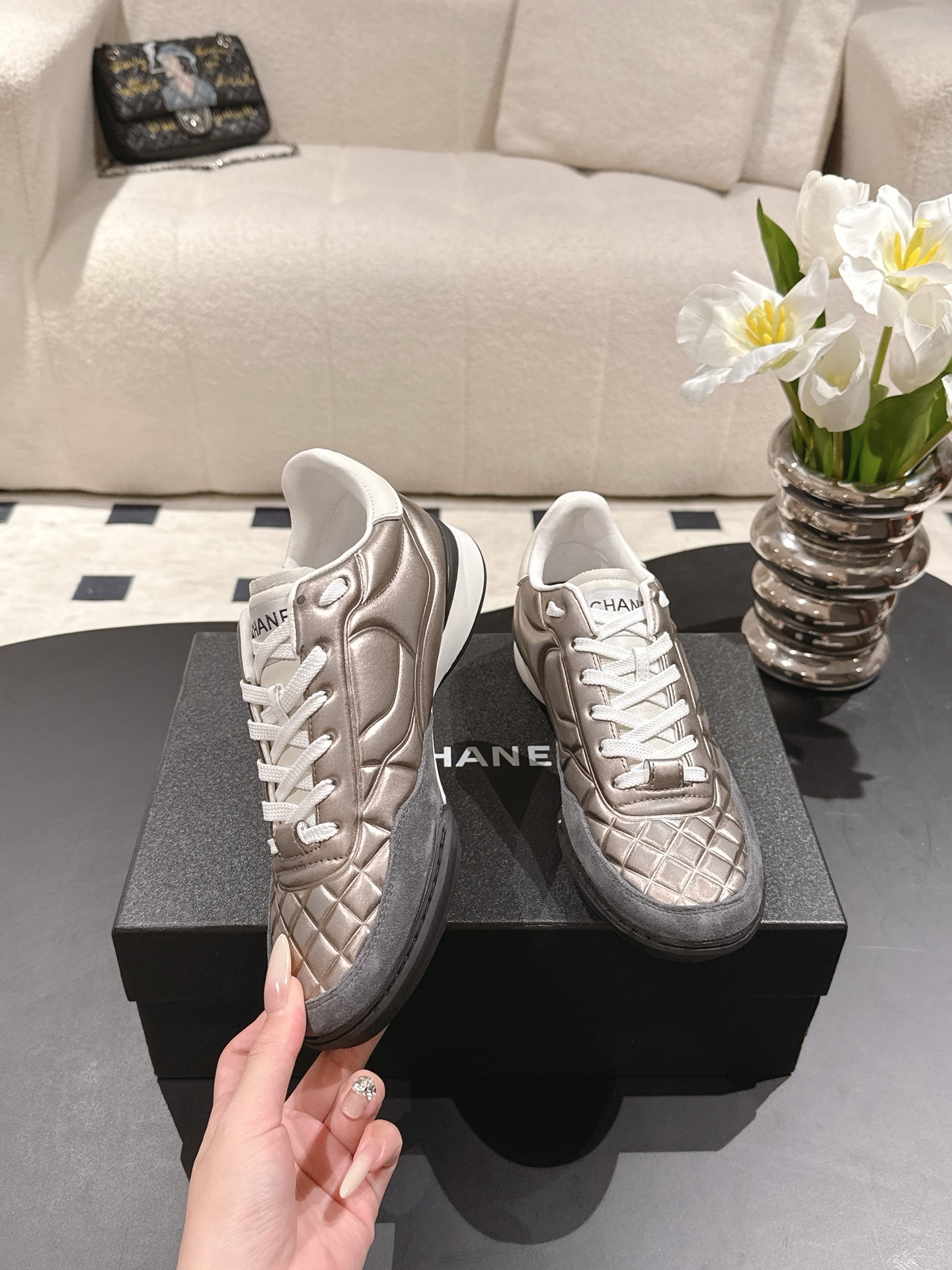 A pair of Chanel quilted metallic leather sneakers in champagne bronze resting on a black designer box - Hình 4