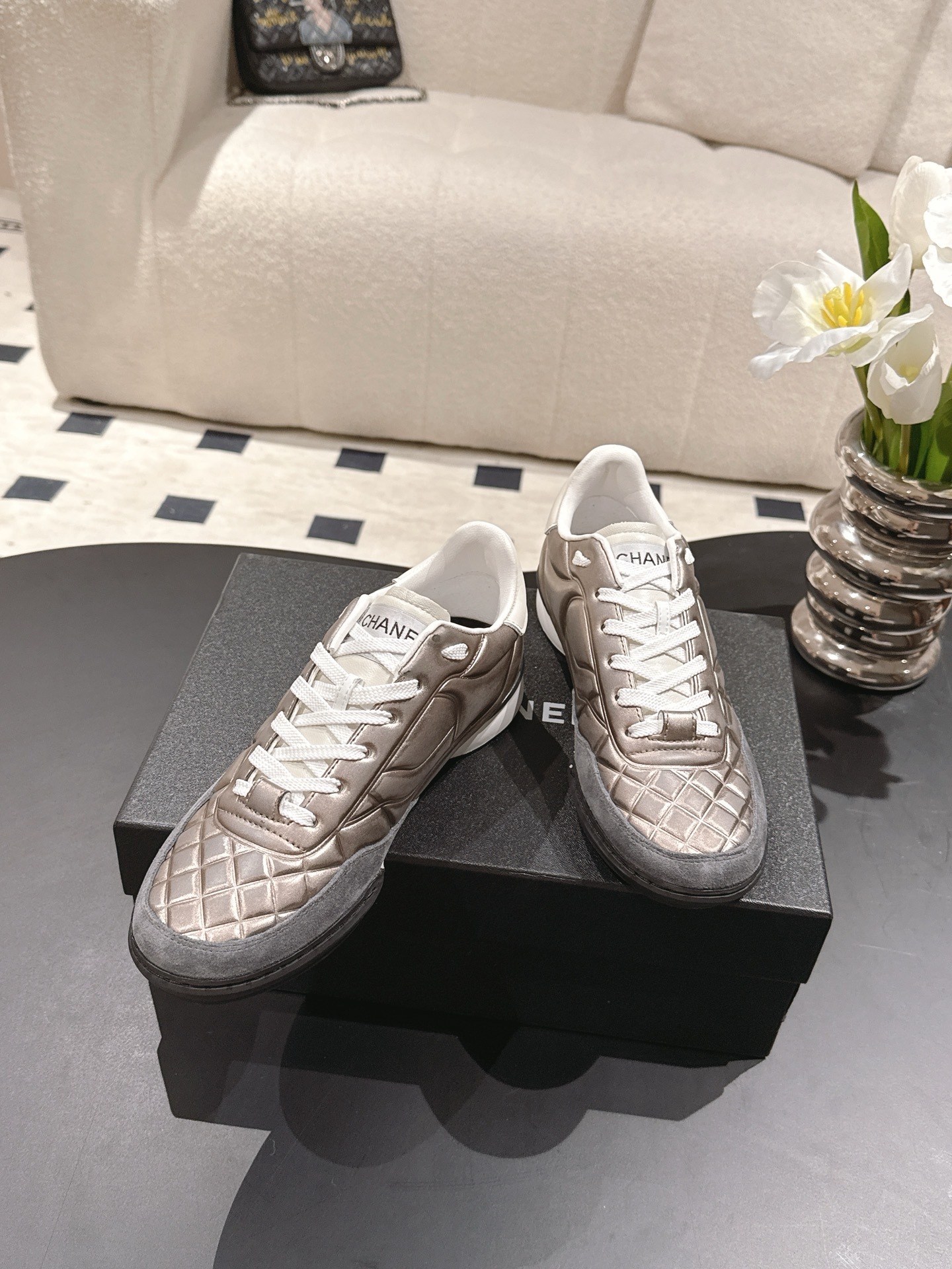 A pair of Chanel quilted metallic leather sneakers in champagne bronze resting on a black designer box - Hình 3