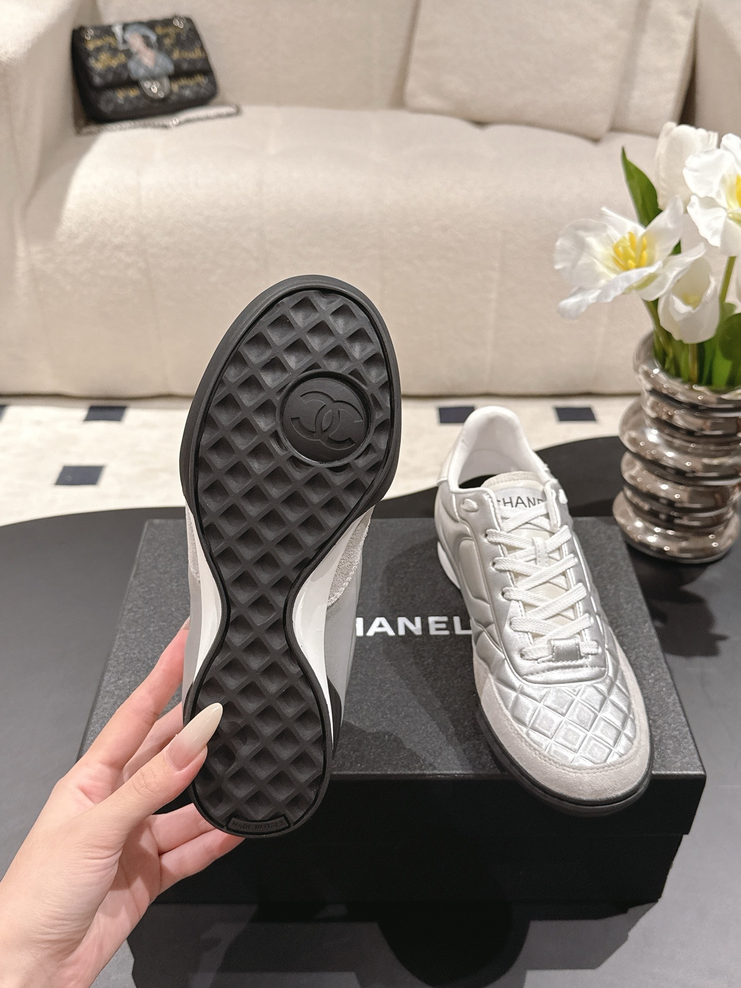 A pair of luxury Chanel metallic silver quilted sneakers displayed on a black designer shoebox - Hình 10