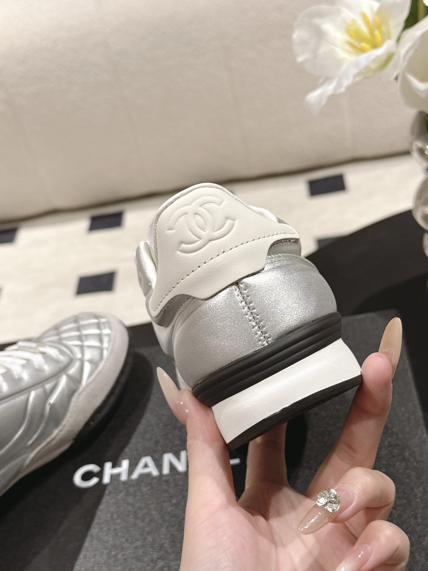 A pair of luxury Chanel metallic silver quilted sneakers displayed on a black designer shoebox - Hình 9