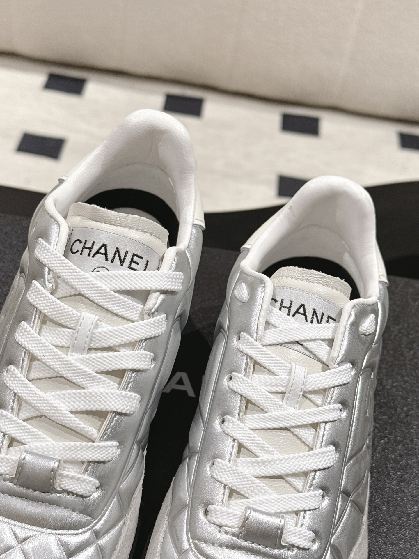 A pair of luxury Chanel metallic silver quilted sneakers displayed on a black designer shoebox - Hình 7
