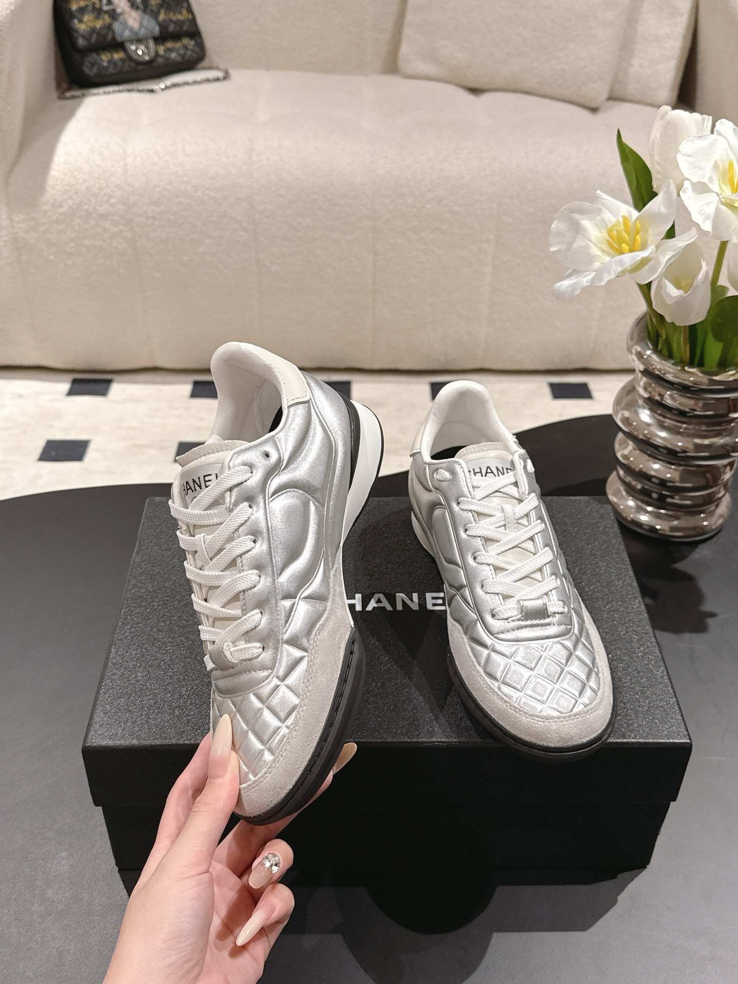 A pair of luxury Chanel metallic silver quilted sneakers displayed on a black designer shoebox - Hình 6