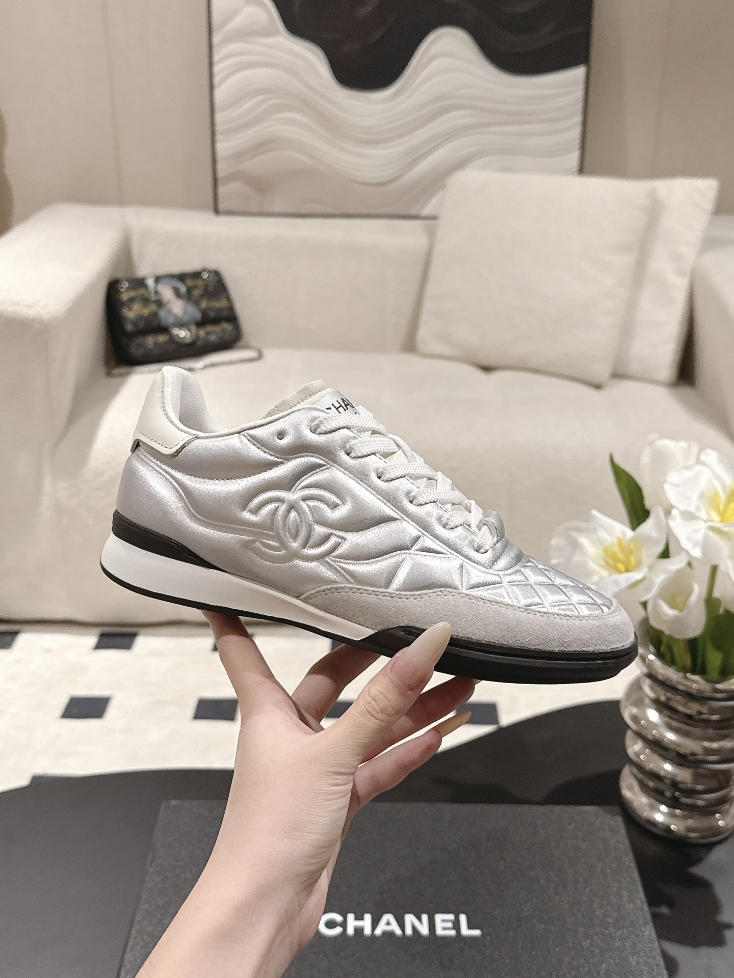 A pair of luxury Chanel metallic silver quilted sneakers displayed on a black designer shoebox - Hình 5