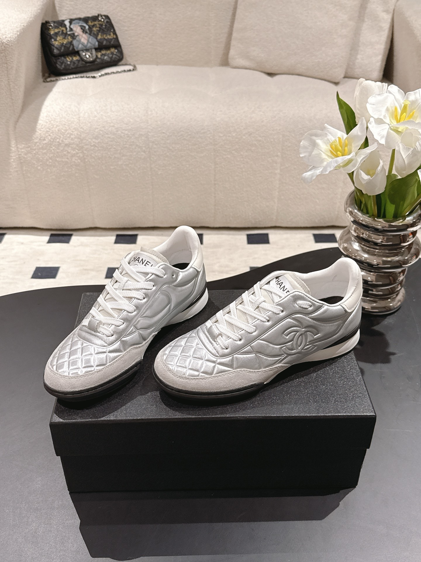 A pair of luxury Chanel metallic silver quilted sneakers displayed on a black designer shoebox - Hình 3