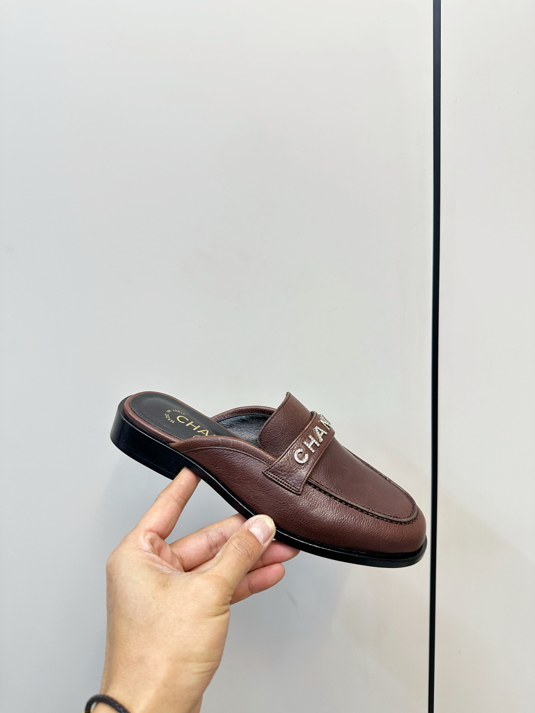 Pair of brown Chanel leather mules with crystal logo lettering displayed on a black box. - Hình 4