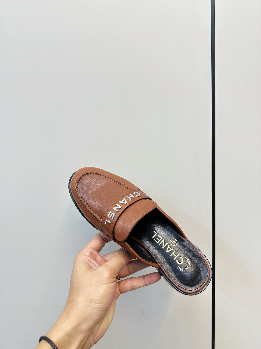 A pair of Chanel brown leather mules with crystal-embellished logo on a black designer box - Hình 9