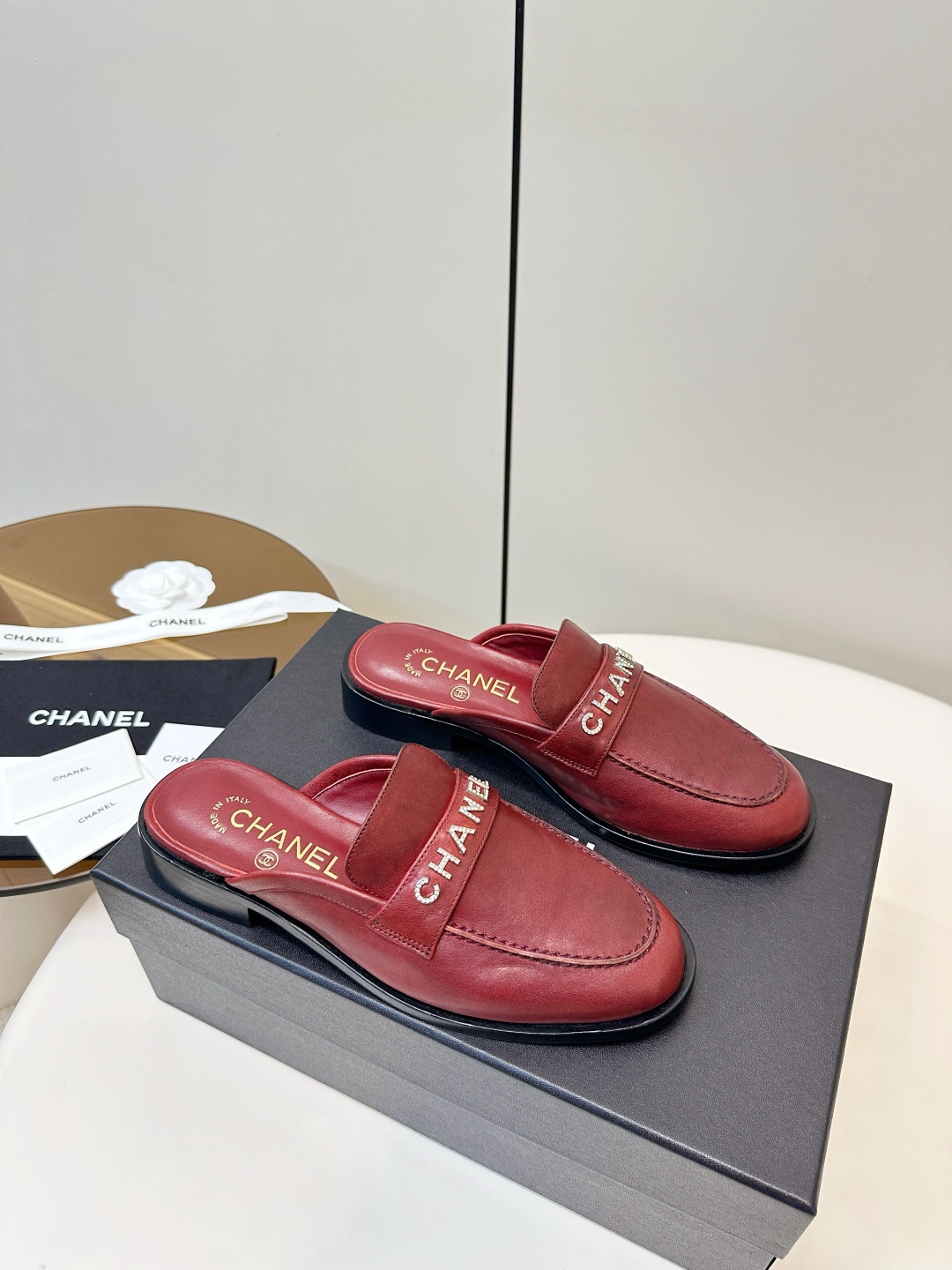 Luxury Chanel burgundy leather mules with crystal-embellished logo displayed on a black Chanel box. - Hình 3